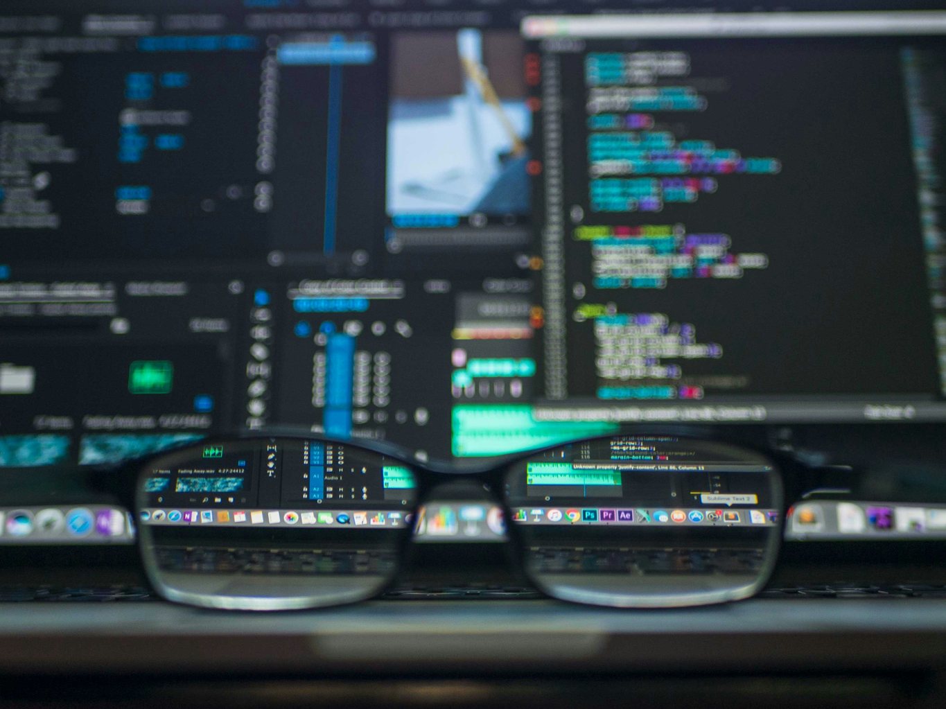 A monitor displaying dense technical text beside a notepad on a plain desk