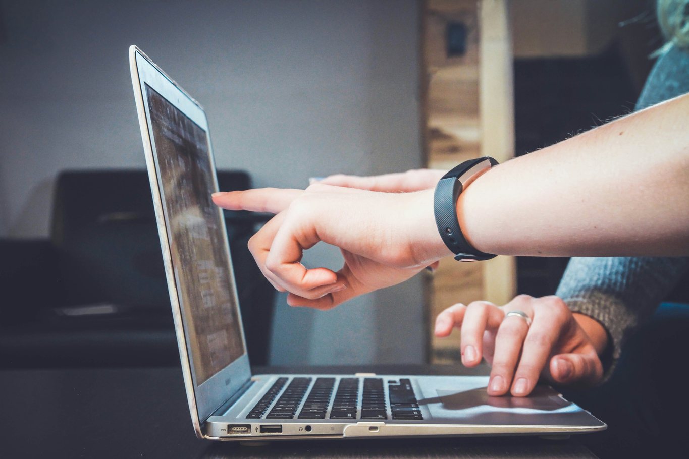 Two hands at a laptop, one finger pointing to text on the screen