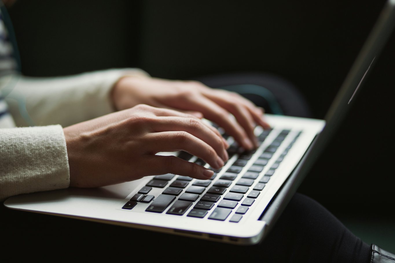 A person's hands typing on a laptop keyboard in low light